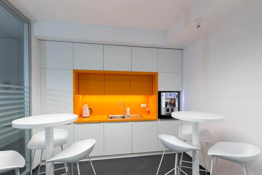 Modern office kitchenette with white cabinets and orange accents for business spaces.